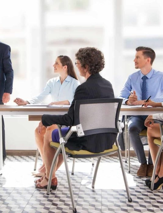 Smiling senior businessman conducting presentation in front of coworkers. Aged financial manager explaining new strategy to colleagues.Business presentation concept